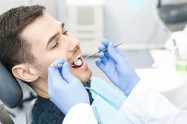 Smiling patient sitting in dental chair receiving exam from dentist