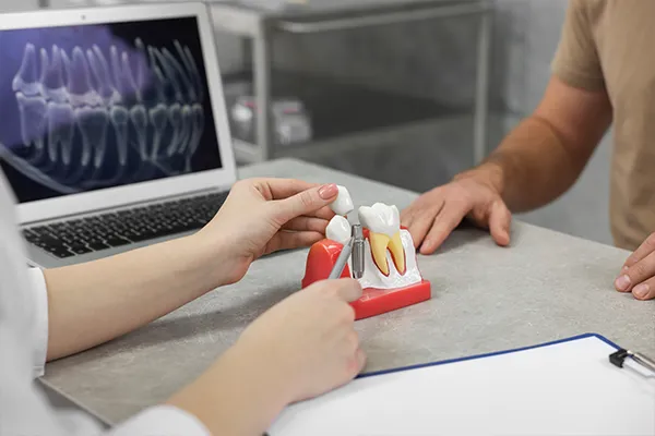 A dentist using a dental implant model to explain the procedure to a patient at  Rolling Plains Dentistry in Quanah, TX